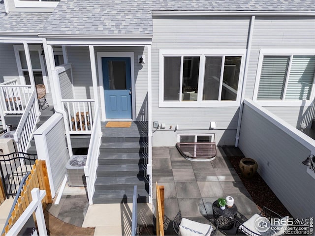 view of exterior entry featuring central AC and roof with shingles