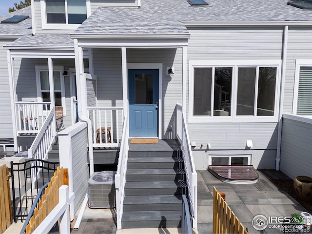 doorway to property featuring a porch, cooling unit, roof with shingles, and fence