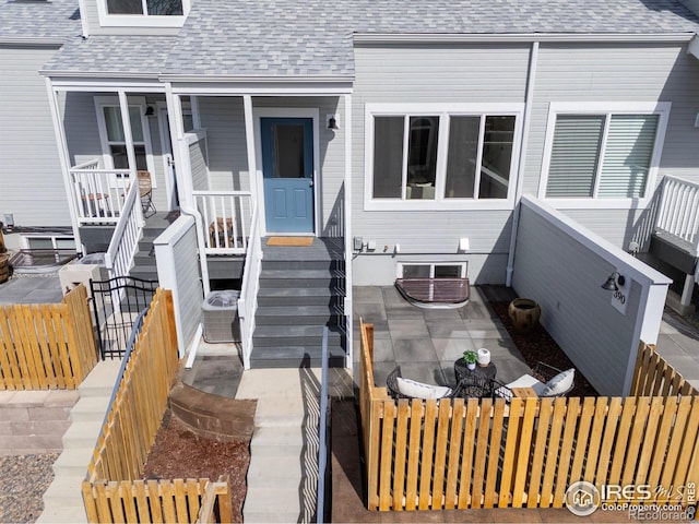 doorway to property with a patio area, fence, and a shingled roof