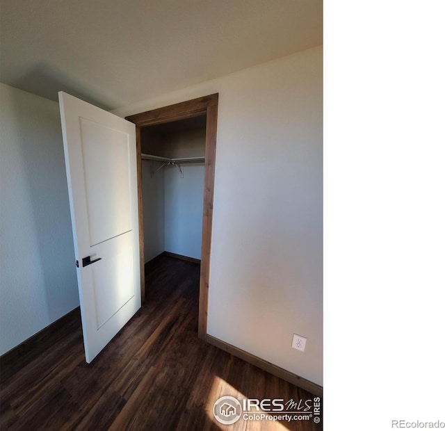 unfurnished bedroom featuring a closet, dark wood-type flooring, and baseboards