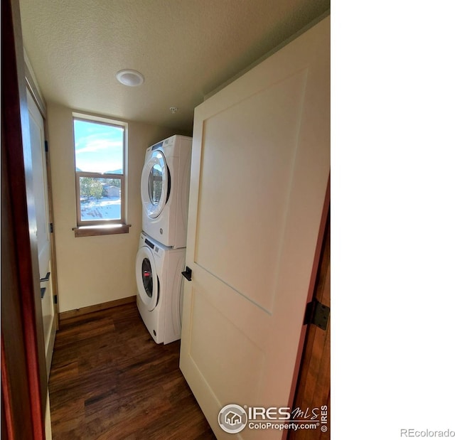 laundry area featuring a textured ceiling, laundry area, stacked washer / drying machine, and dark wood-type flooring