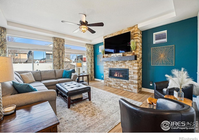 living area with a raised ceiling, wood finished floors, a fireplace, baseboards, and ceiling fan