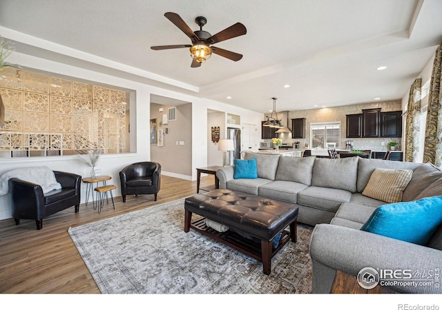 living area with a raised ceiling, light wood-style flooring, and baseboards