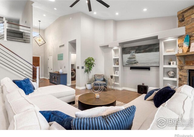 living area featuring visible vents, washer / clothes dryer, wood finished floors, stairway, and a stone fireplace