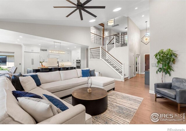 living room with high vaulted ceiling, a ceiling fan, recessed lighting, light wood finished floors, and stairs