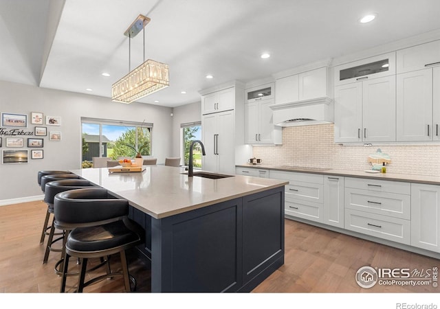 kitchen featuring a sink, stovetop, white cabinets, and light wood-style flooring