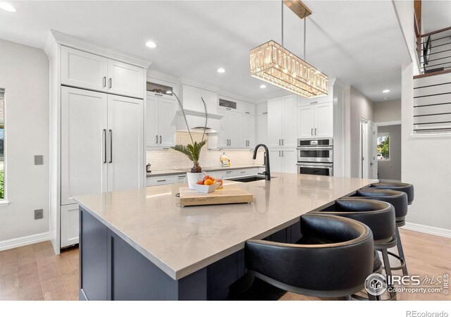 kitchen with a sink, plenty of natural light, backsplash, stainless steel double oven, and white cabinets