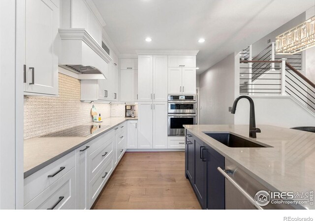 kitchen featuring decorative backsplash, appliances with stainless steel finishes, light wood-style floors, white cabinetry, and a sink