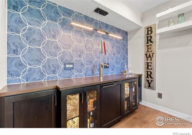 bar with light wood-type flooring, baseboards, beverage cooler, and a dry bar