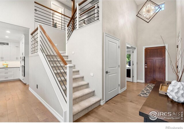 foyer featuring light wood finished floors, baseboards, and a towering ceiling