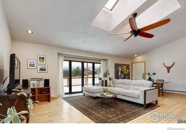 living area featuring hardwood / wood-style floors, recessed lighting, vaulted ceiling with skylight, baseboard heating, and ceiling fan