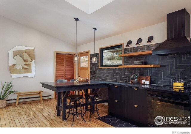 bar with oven, a baseboard heating unit, wall chimney exhaust hood, light wood finished floors, and vaulted ceiling