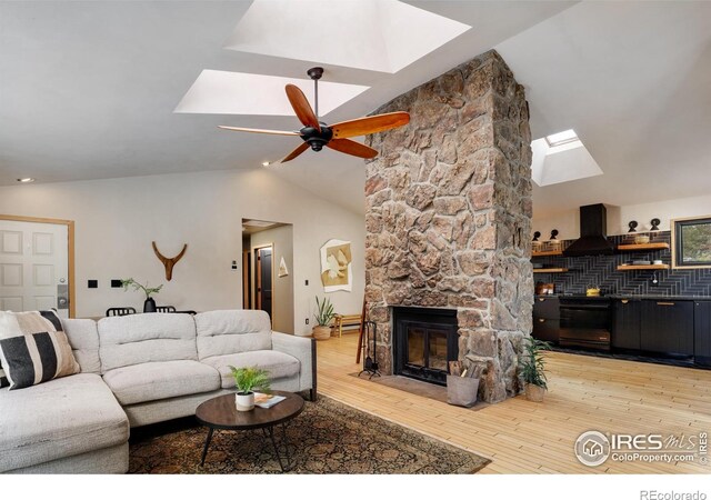 living area featuring a ceiling fan, light wood finished floors, high vaulted ceiling, a skylight, and a fireplace