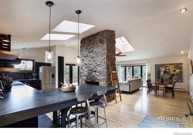 dining room with lofted ceiling with skylight, a stone fireplace, and light wood-style flooring