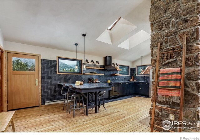 kitchen featuring light wood finished floors, vaulted ceiling with skylight, hanging light fixtures, extractor fan, and backsplash