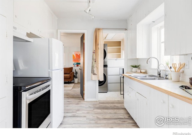 kitchen with under cabinet range hood, stainless steel electric range oven, light countertops, stacked washer / drying machine, and a sink