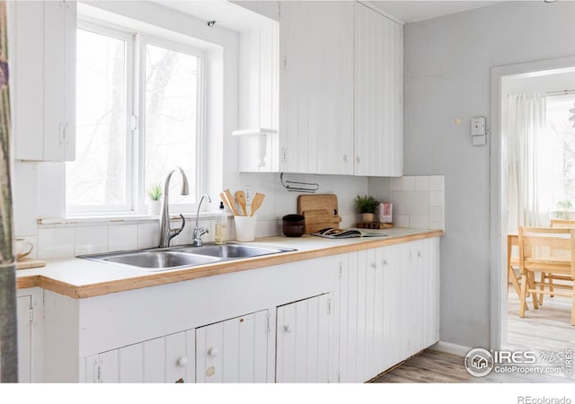 kitchen with light wood-style flooring, white cabinetry, light countertops, and a sink