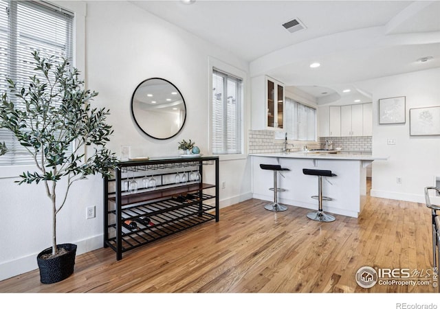 interior space featuring light wood-type flooring, visible vents, a kitchen bar, and a healthy amount of sunlight