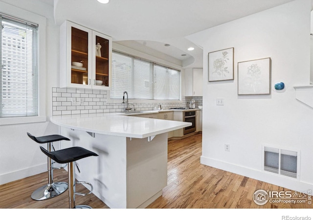 kitchen with visible vents, a kitchen bar, light wood-style floors, and a peninsula