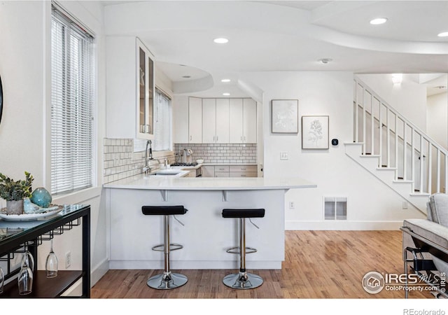 kitchen with tasteful backsplash, visible vents, light countertops, light wood-style flooring, and a sink