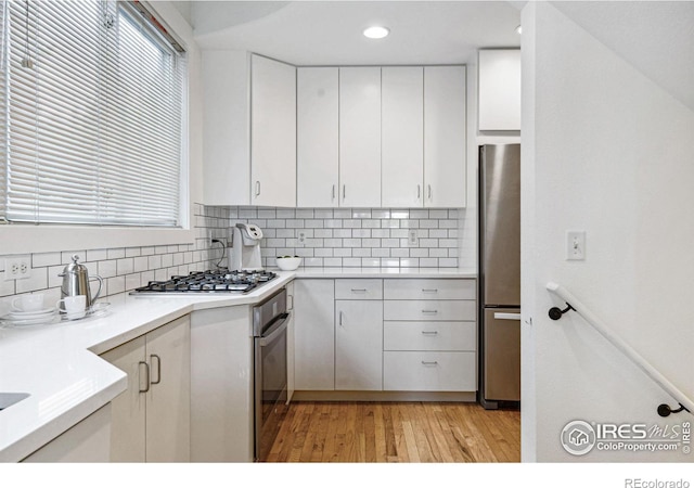 kitchen featuring backsplash, light wood-style floors, appliances with stainless steel finishes, and white cabinetry