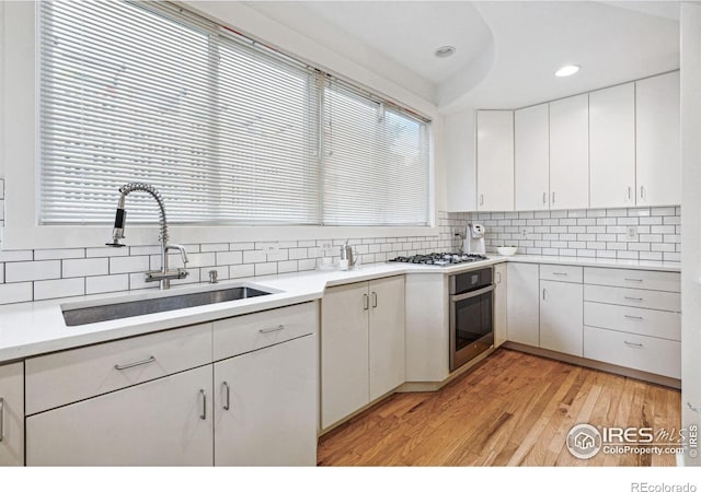 kitchen featuring light wood-style flooring, a sink, tasteful backsplash, white cabinetry, and stainless steel appliances