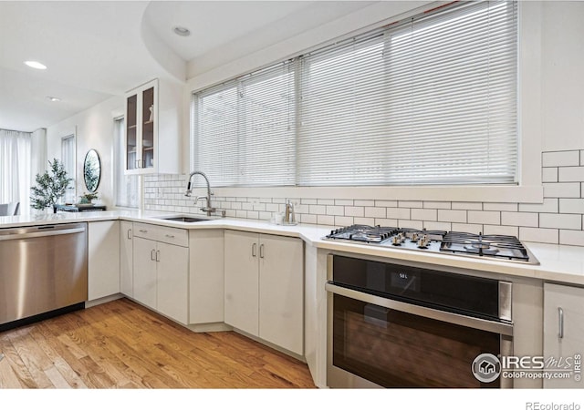 kitchen with a sink, stainless steel appliances, light wood-style floors, and white cabinets