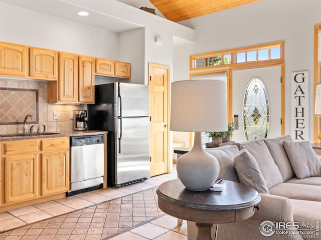 kitchen with a sink, light stone counters, open floor plan, appliances with stainless steel finishes, and decorative backsplash