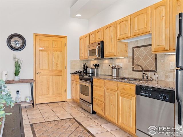 kitchen with light brown cabinetry, a sink, stone countertops, appliances with stainless steel finishes, and decorative backsplash