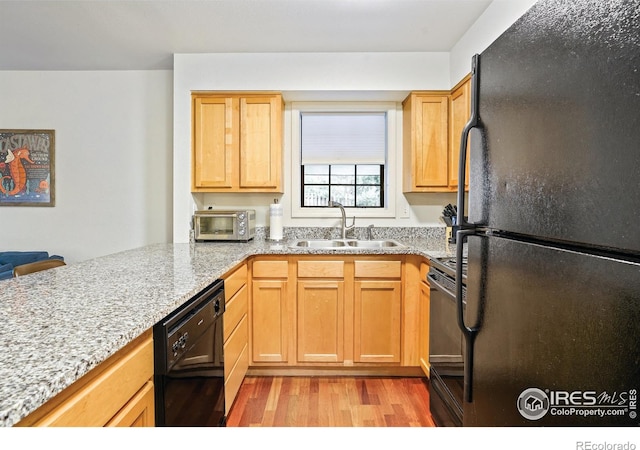 kitchen with light stone countertops, a toaster, a sink, black appliances, and light wood-type flooring