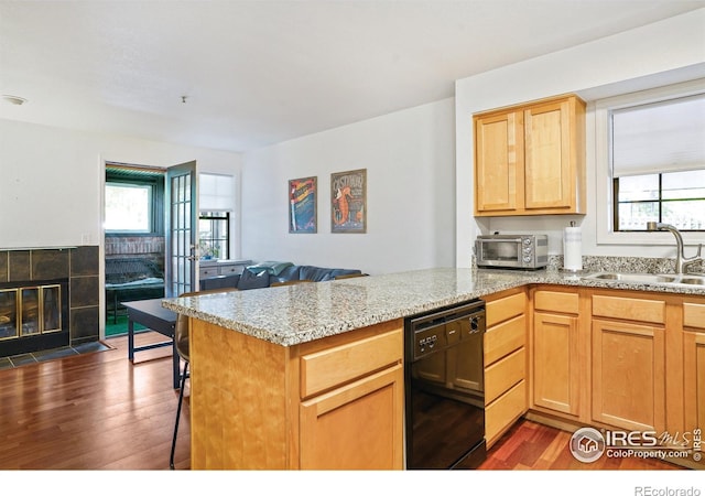 kitchen featuring a tiled fireplace, dishwasher, a peninsula, dark wood-style floors, and a sink