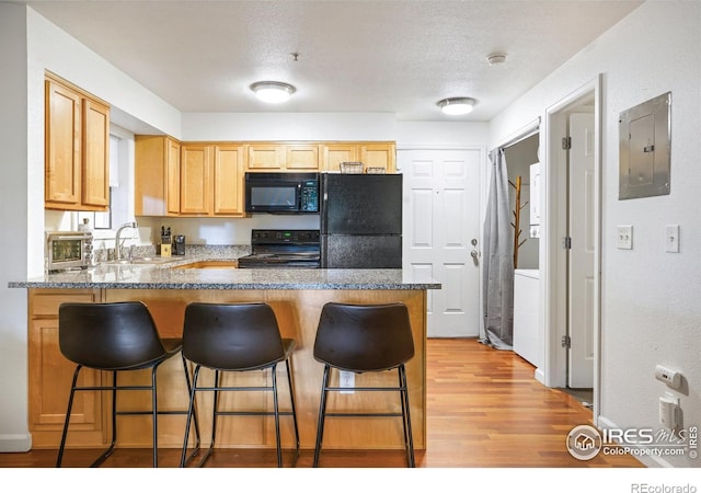 kitchen with electric panel, a peninsula, a sink, black appliances, and light wood finished floors