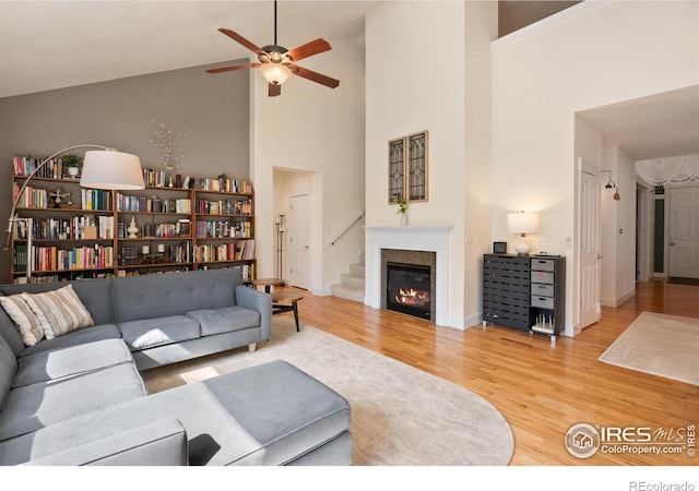 living area with wood finished floors, baseboards, a high ceiling, ceiling fan, and a glass covered fireplace