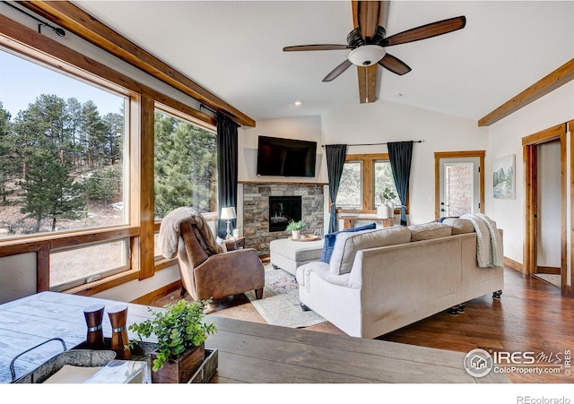 living room featuring wood finished floors, baseboards, vaulted ceiling with beams, ceiling fan, and a stone fireplace