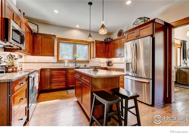 kitchen featuring light stone countertops, light wood finished floors, a kitchen island, stainless steel appliances, and tasteful backsplash