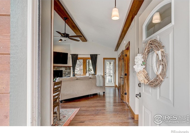 entrance foyer featuring a stone fireplace, lofted ceiling with beams, ceiling fan, and wood finished floors