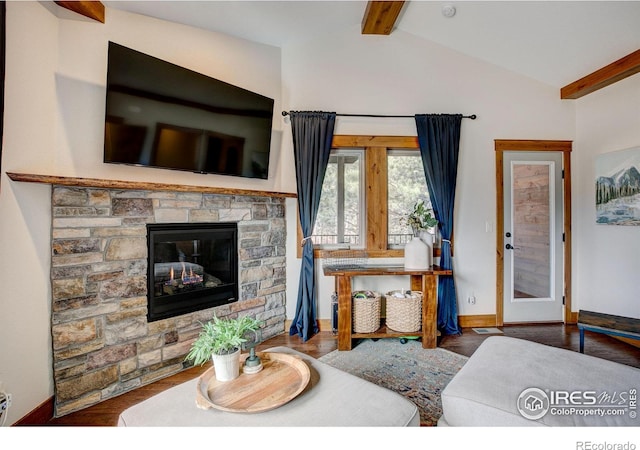 living area featuring baseboards, a stone fireplace, wood finished floors, and vaulted ceiling with beams