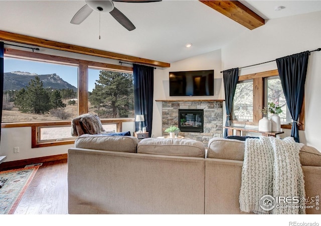 living room featuring wood finished floors, a fireplace, baseboards, ceiling fan, and vaulted ceiling with beams