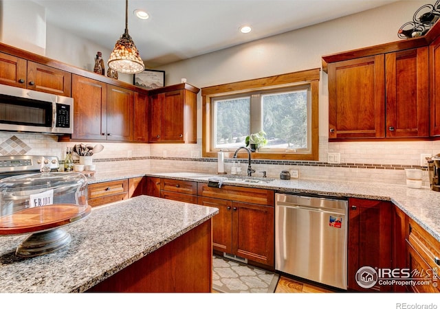 kitchen featuring light stone countertops, a sink, decorative backsplash, hanging light fixtures, and appliances with stainless steel finishes