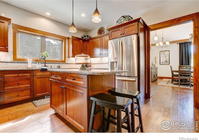 kitchen with light wood finished floors, light stone counters, tasteful backsplash, and stainless steel refrigerator with ice dispenser