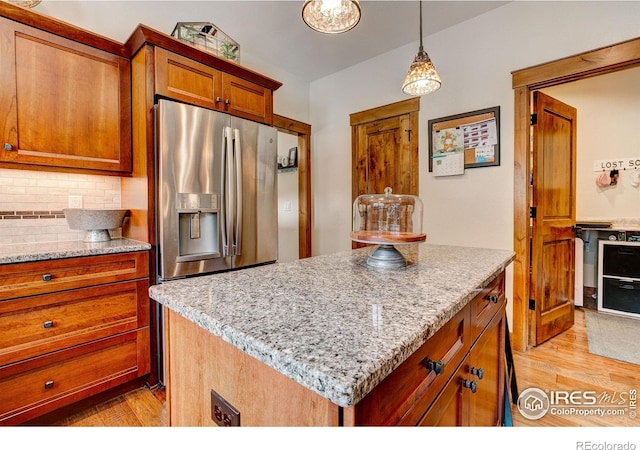 kitchen with stainless steel fridge with ice dispenser, light stone counters, decorative backsplash, light wood-style flooring, and brown cabinetry