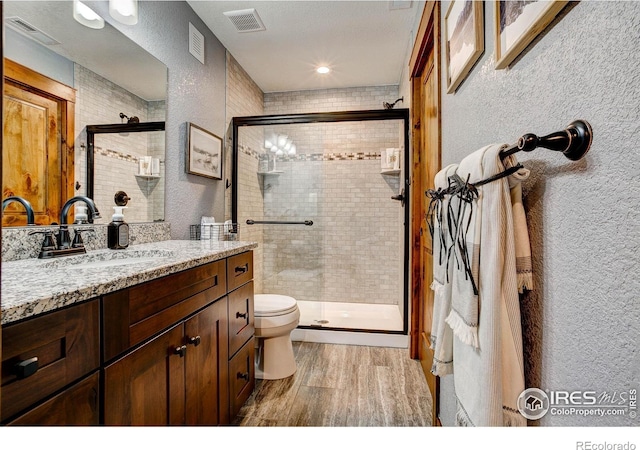 bathroom with wood finished floors, a textured wall, visible vents, and a stall shower