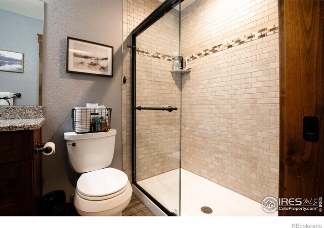 full bath with a stall shower, toilet, vanity, and a textured wall