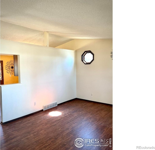 unfurnished room with visible vents, a textured ceiling, dark wood finished floors, baseboards, and vaulted ceiling