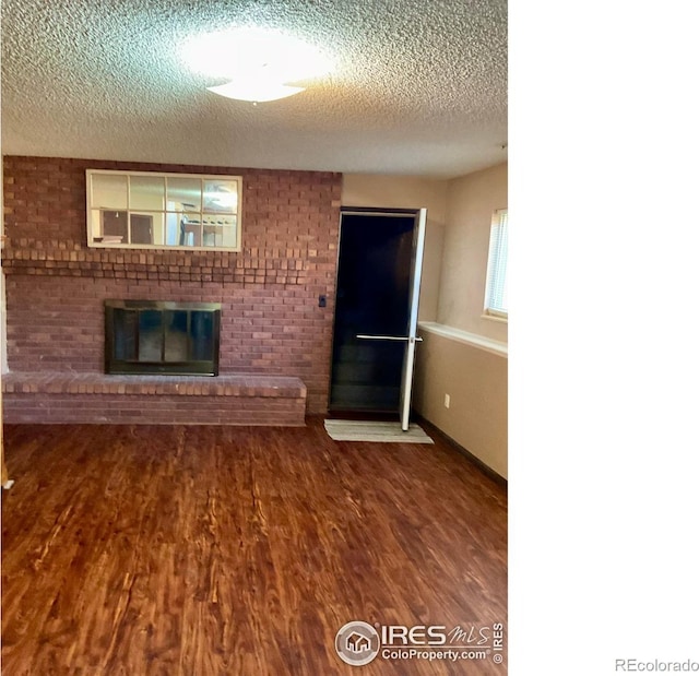 unfurnished living room with a textured ceiling, a brick fireplace, and wood finished floors