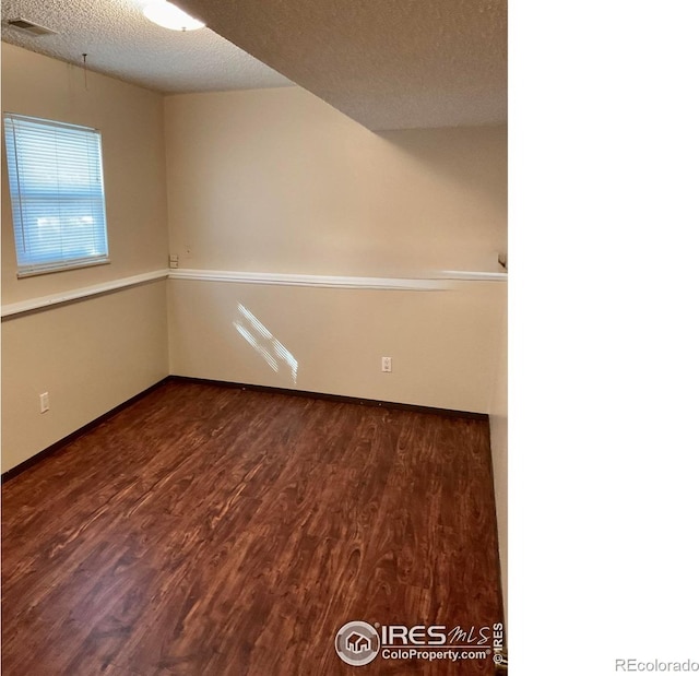 empty room featuring visible vents, a textured ceiling, and dark wood-style flooring