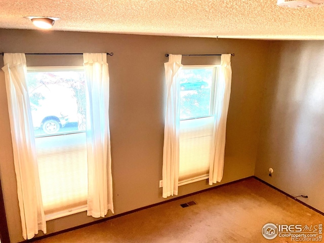 carpeted spare room featuring visible vents, a textured ceiling, and baseboards