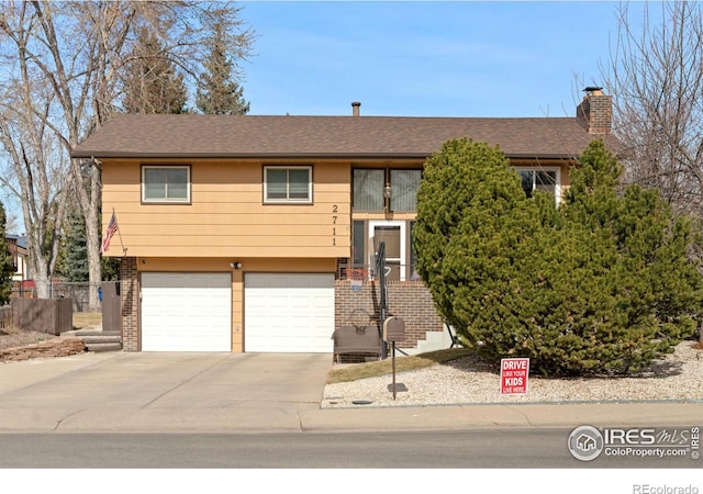 raised ranch featuring a garage, brick siding, concrete driveway, and a chimney