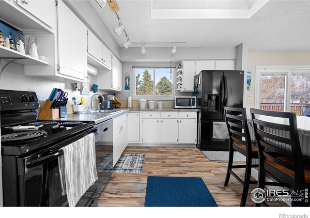 kitchen with black appliances, open shelves, light wood-style flooring, a textured ceiling, and a sink