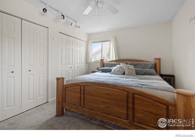 carpeted bedroom with ceiling fan, a textured ceiling, and multiple closets